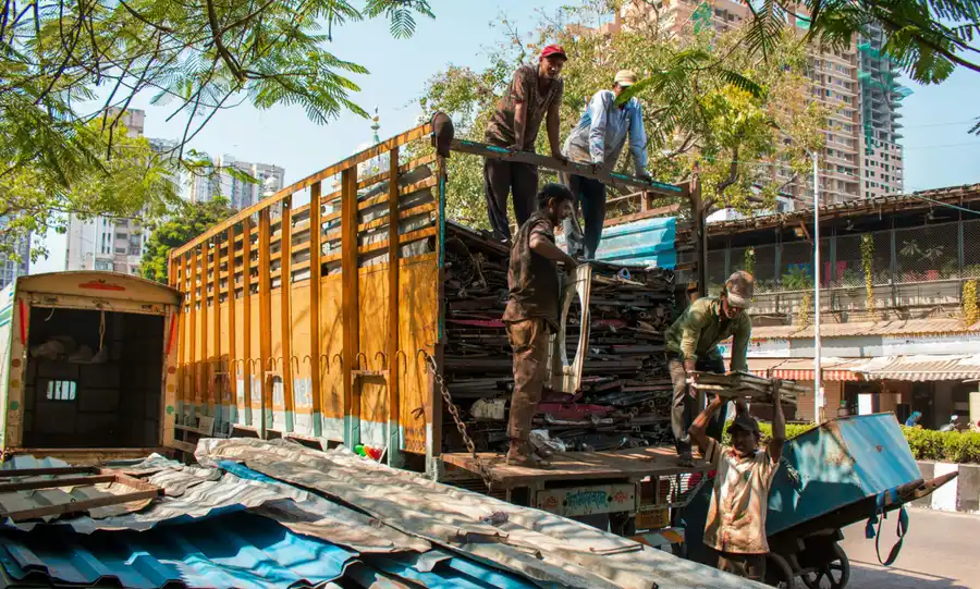 Workers loading scrap metal onto a large yellow truck