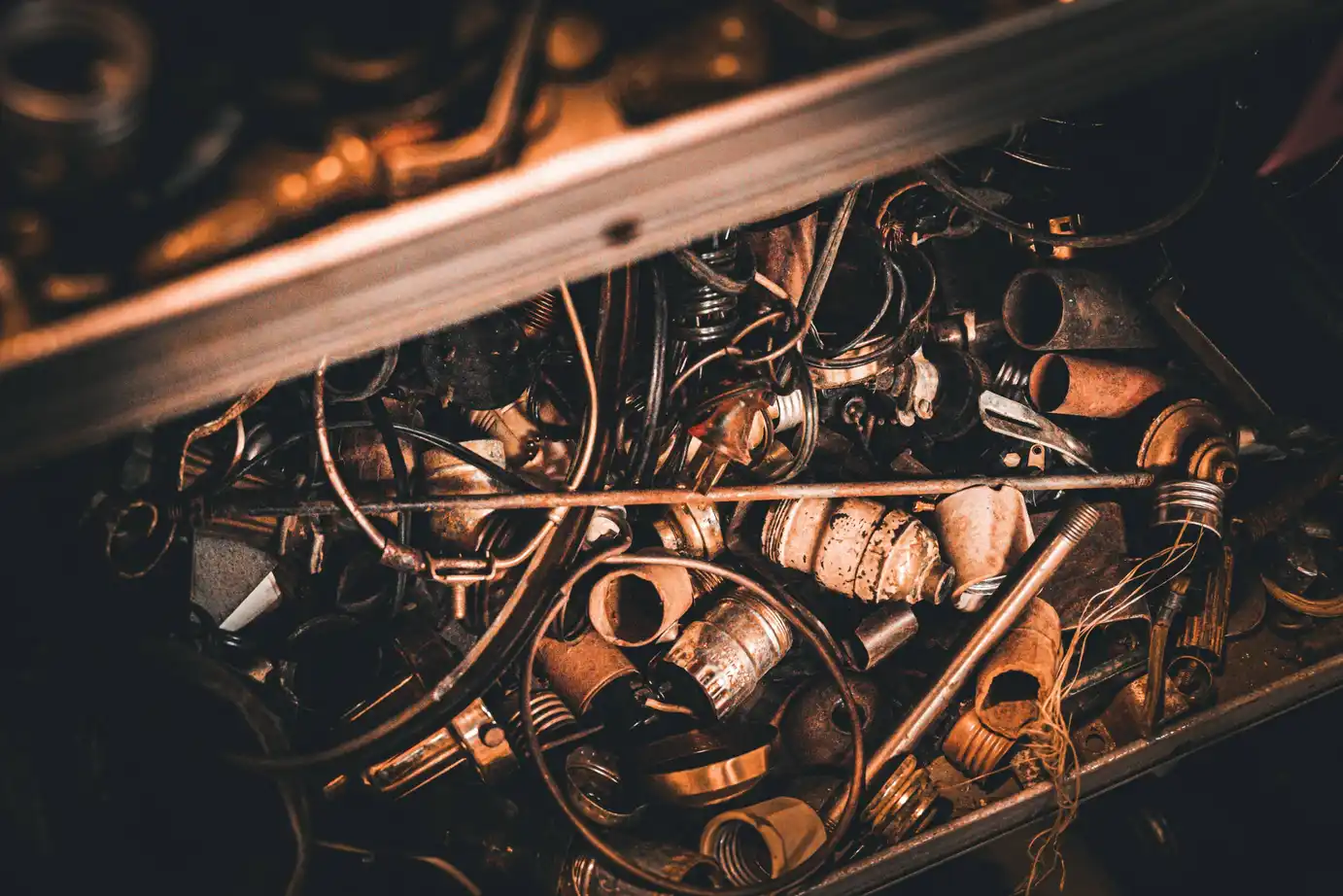 Close-up of tangled rusty metal parts, wires, and old mechanical components in warm, dim light.