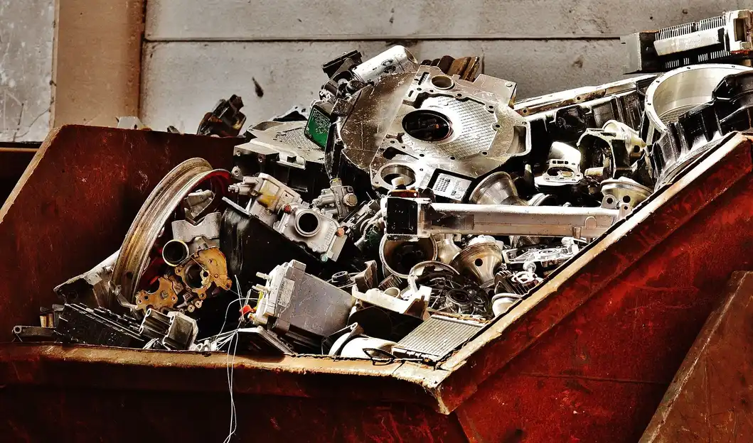 A large rusted metal container filled with discarded mechanical components, including gears, casings, and metal parts in an industrial setting